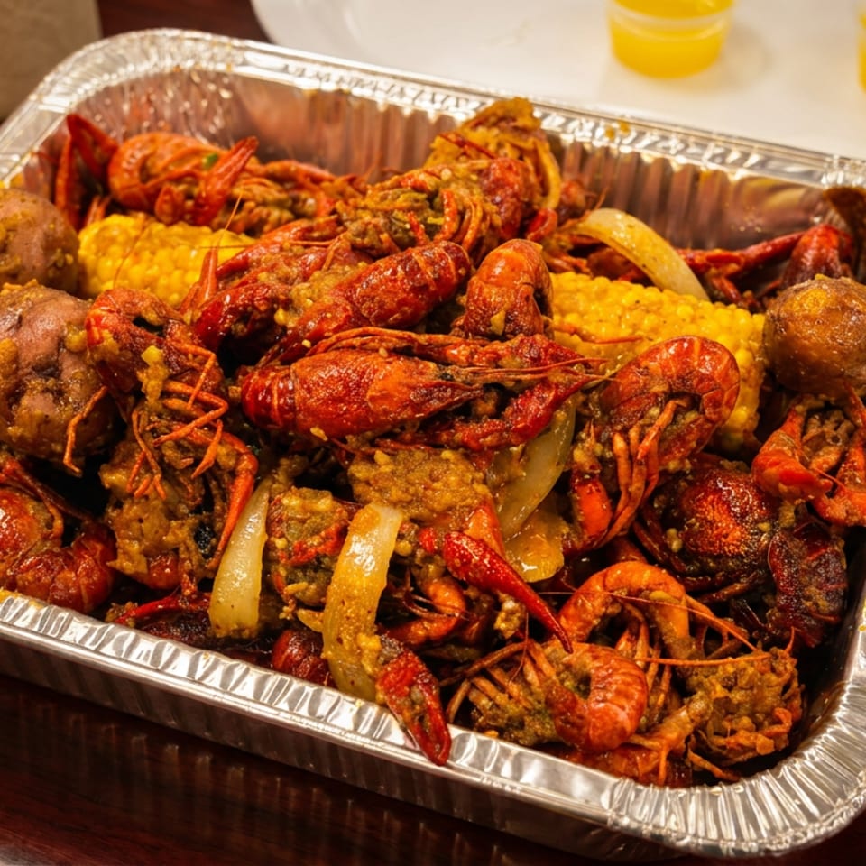 Boiled crawfish, corn, and potatoes in a foil pan on a wooden table.